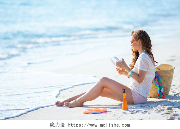 一个年轻漂亮的女人正在海边度假身穿白色T恤和粉色短裤、头戴耳机的年轻女子坐在海滨.